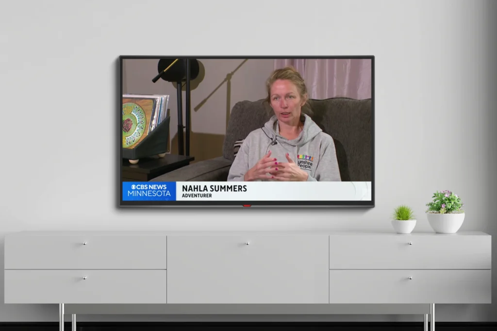 Nahla Summers speaking during a televised interview on a wall-mounted screen above a white sideboard.