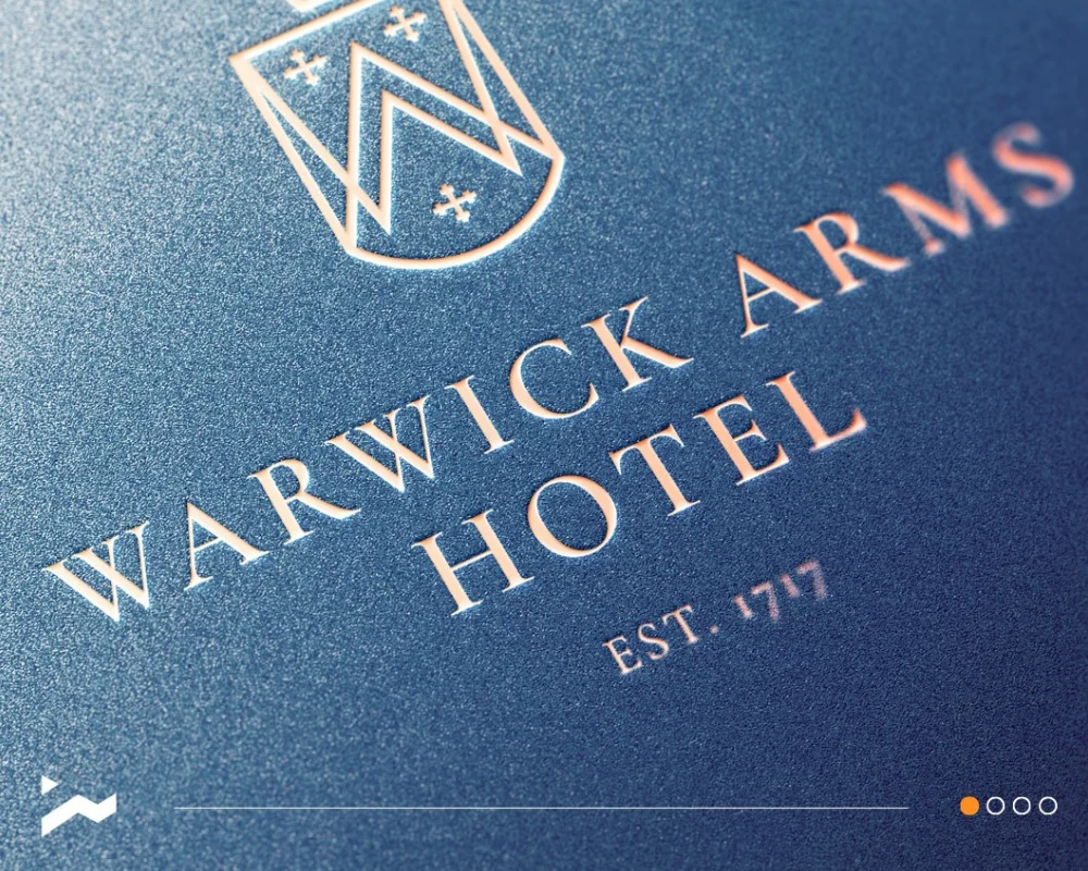 Close-up of the Warwick Arms Hotel crest and lettering on a textured blue background, marked Est. 1777