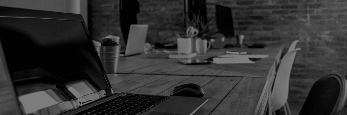 Black-and-white office workspace with an open laptop, mouse, coffee cup, desks and chairs